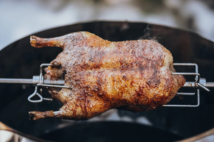Goldbraune Ente mit knuspriger Haut am Drehspieß über dem Kugelgrill