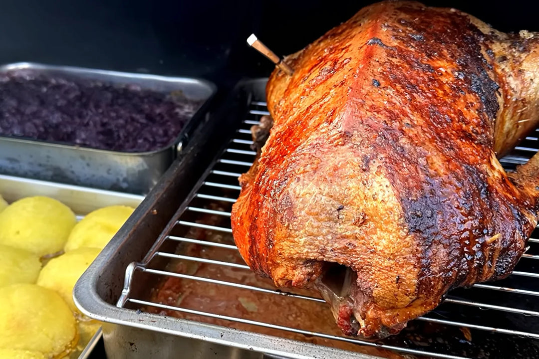 Goldbraune Gans auf dem Rost im Pelletgrill, daneben Rotkohl und Kartoffelklöße