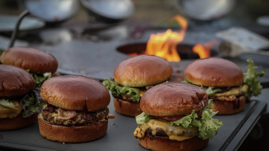 Mehrere Classic Burger mit Käse und Salat auf der Ablage des BANDIT 2.0, im Hintergrund Feuer