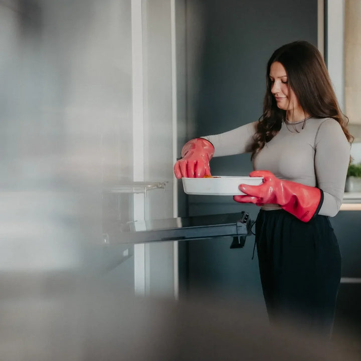Mit roten MOESTA HEATPRO eine Auflaufform am geöffneten Backofen halten