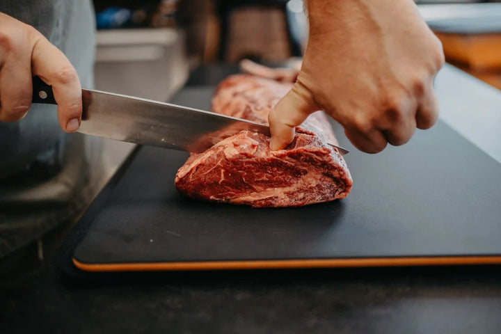 Fleisch wird auf einem schwarzen MOESTA JOE Schneidebrett aus PaperPlank geschnitten.