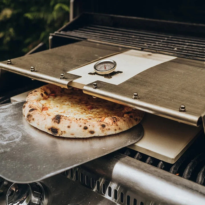 Gebackene Pizza auf dem Pizzaschieber vor dem LORENZO Pizzacover auf dem Gasgrill
