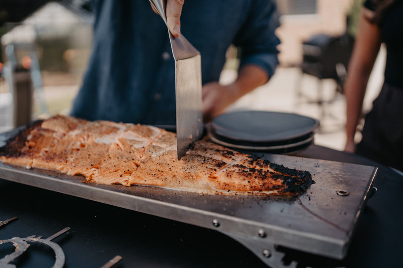 Fertig gegrillter Flammlachs wird mit einem Spachtel portioniert