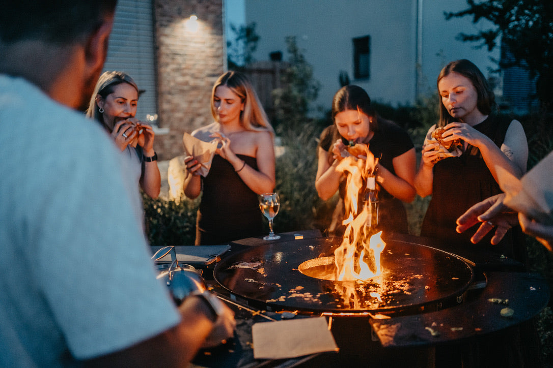 Gäste essen gemeinsam Burger rund um das Feuer des BANDIT
