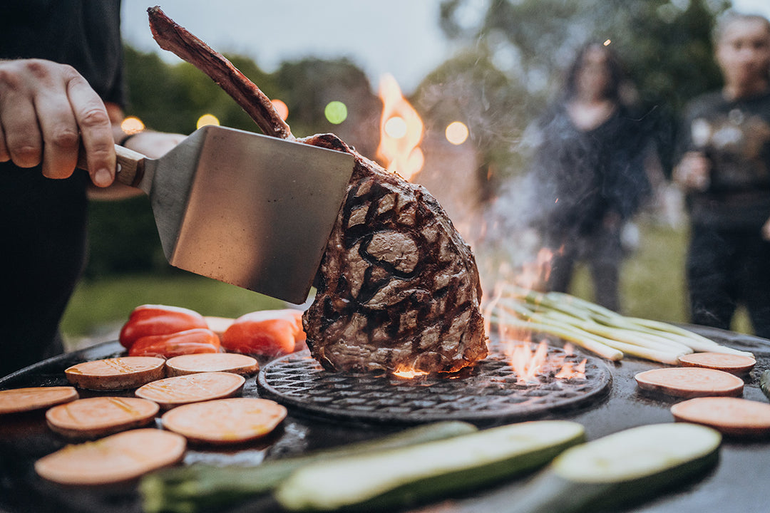 Steak mit MOESTA-Stier-Branding auf dem Sizzle-Rost in der Barbecue-Disc; Gemüse brät auf der umliegenden Feuerplatte.