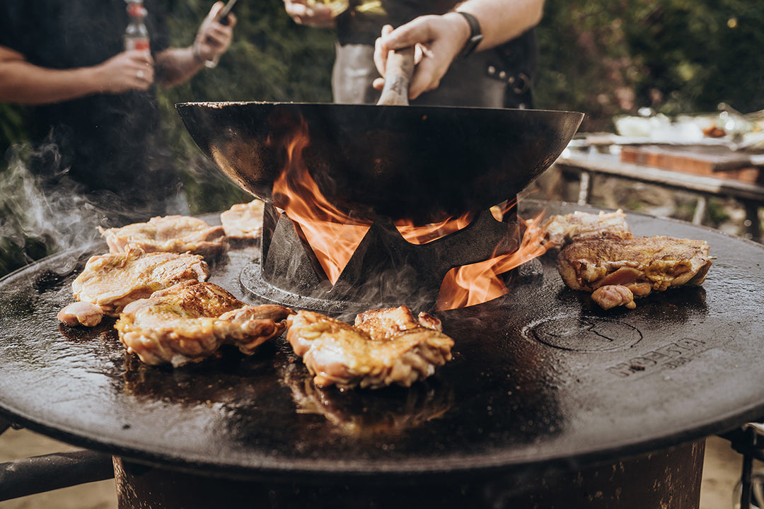 Wok auf der Wok-Krone in der mittigen Öffnung der Barbecue-Disc, umgeben von Grillgut auf der Feuerplatte.