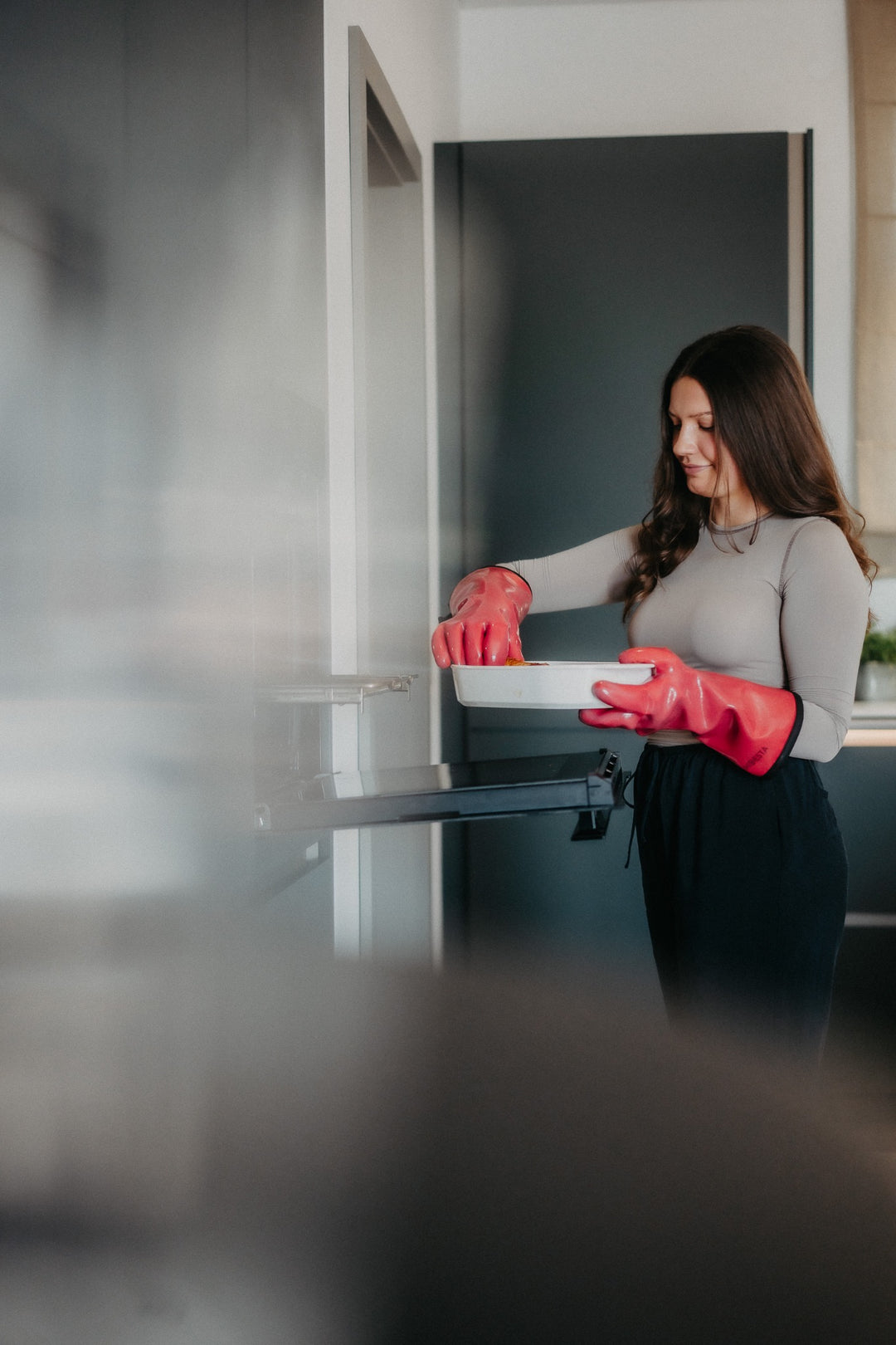 Eine Frau hält mit roten HEATPRO Hitzehandschuhen eine Auflaufform vor dem geöffneten Backofen.