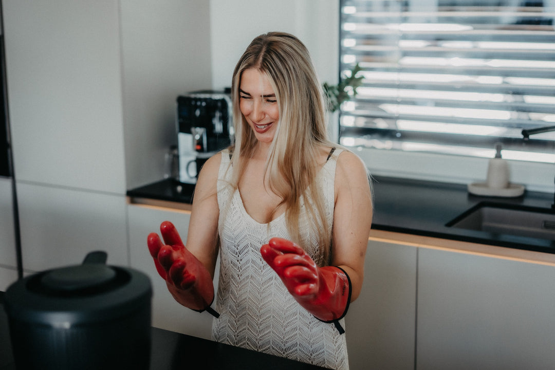 Eine Frau trägt rote HEATPRO Hitzehandschuhe in ihrer Küche.