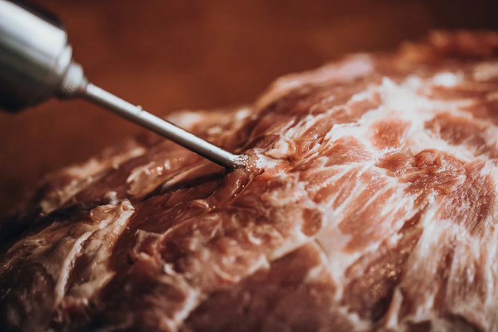 Marinade wird mit einer Bratenspritze in rohes Fleisch injiziert